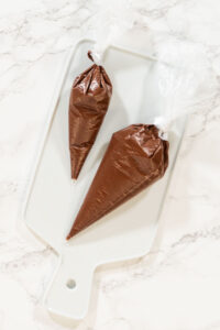 Rich Chocolate Royal Icing for Decorating - Arina Photography Piping Bags on Cooling Rack Description: Overhead view of piping bags filled with melted chocolate resting on a cooling rack, prepared for the Chocolate Royal Icing recipe.