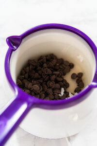 Rich Chocolate Royal Icing for Decorating - Arina Photography Chocolate Chips and Coconut Oil in Melting Pot Description: Overhead view of chocolate chips and coconut oil in a purple melting pot, prepared for melting into a smooth chocolate royal icing.